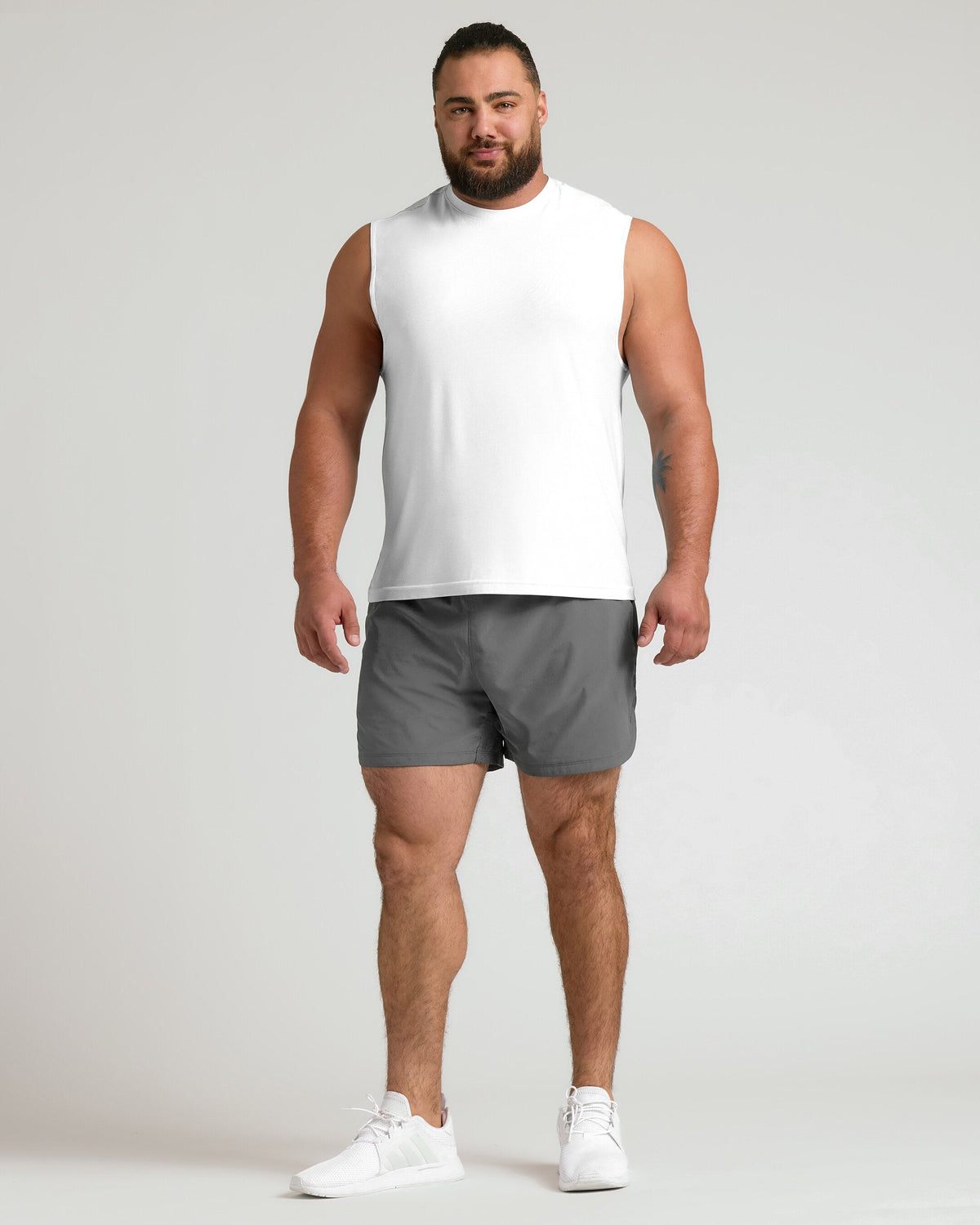 Man in White Sleeveless Active Muscle Tee, gray shorts, white sneakers.