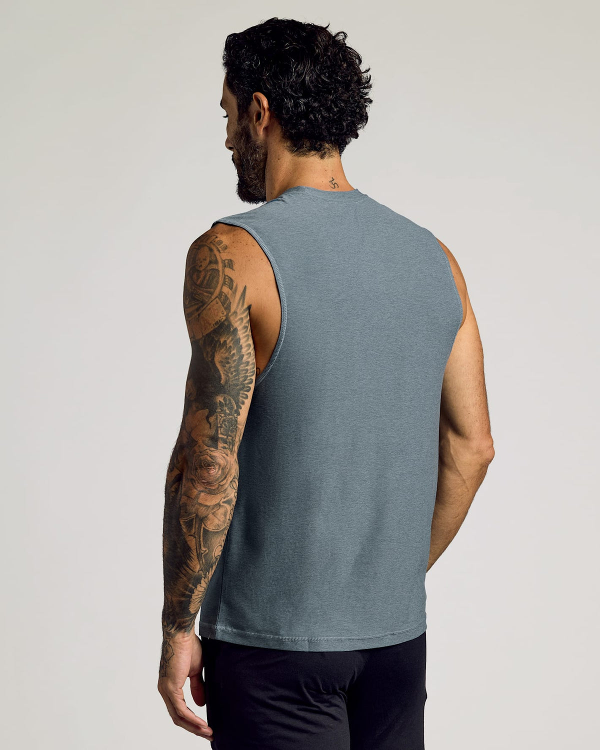 Man wearing a heather navy sleeveless shirt showing back tattoos, displaying the Sleeveless Active Muscle Tee 3-Pack as a comfortable men's basics option.