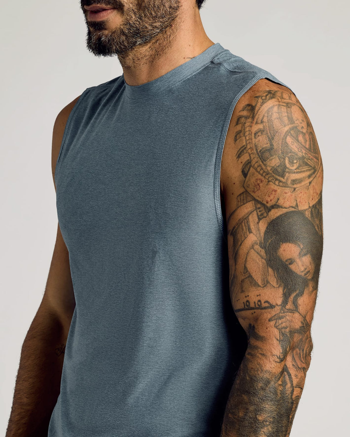 Close-up of a man wearing a heather navy sleeveless active muscle tee 3-pack, showcasing his detailed arm tattoo and the muscle fit of the men's basic shirt.