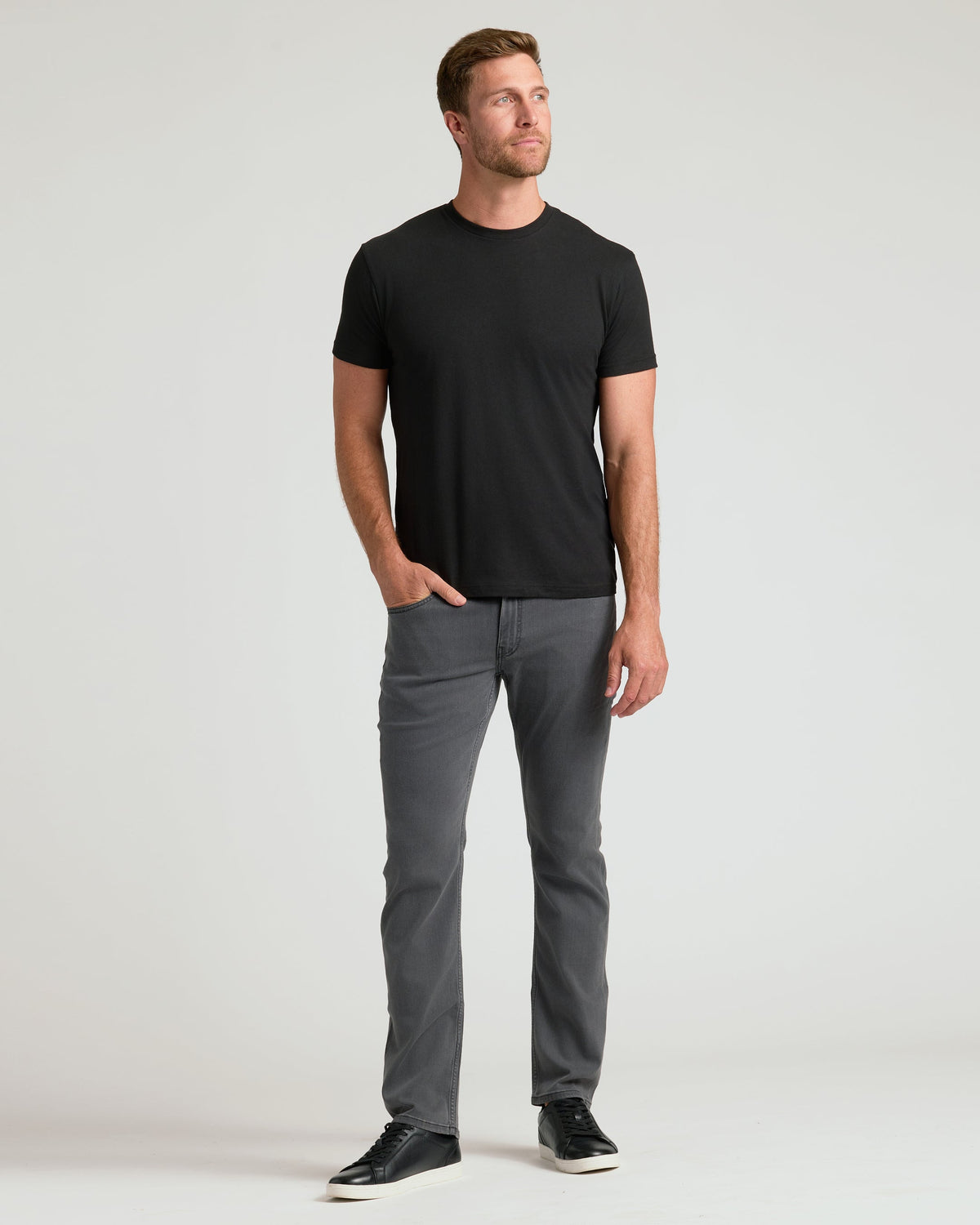 Black crew neck t-shirt with short sleeves, paired with gray jeans and black sneakers.