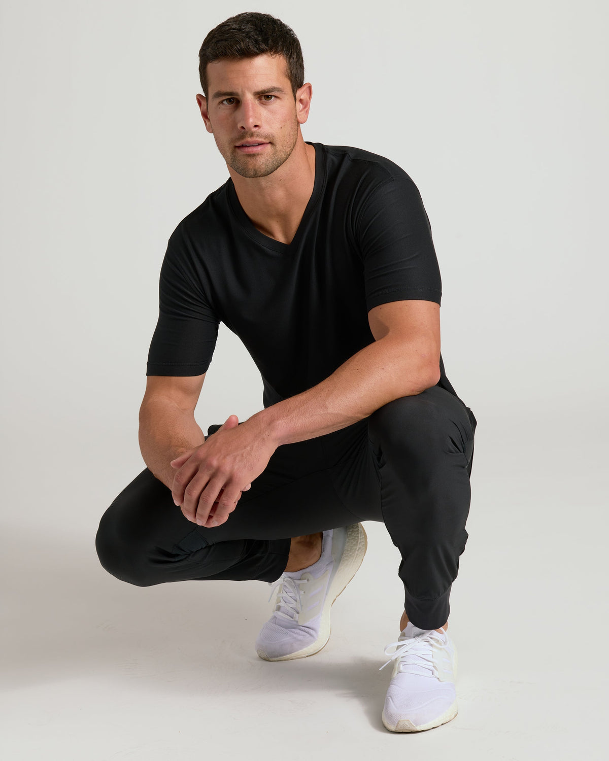 Young man wearing Black Active V-Neck, joggers, and white running shoes.