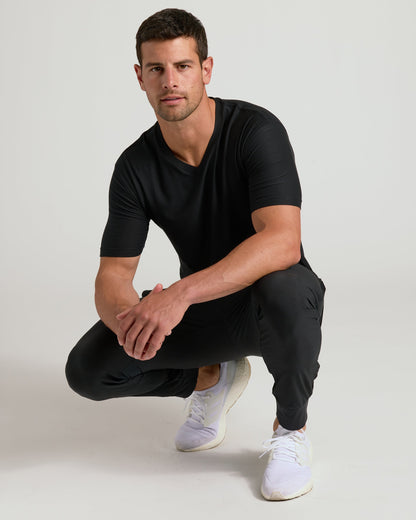 Young man wearing Black Active V-Neck, joggers, and white running shoes.